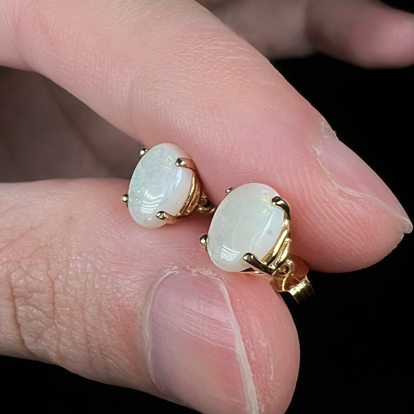 Real opal earrings in gold, angled close-up in fingers