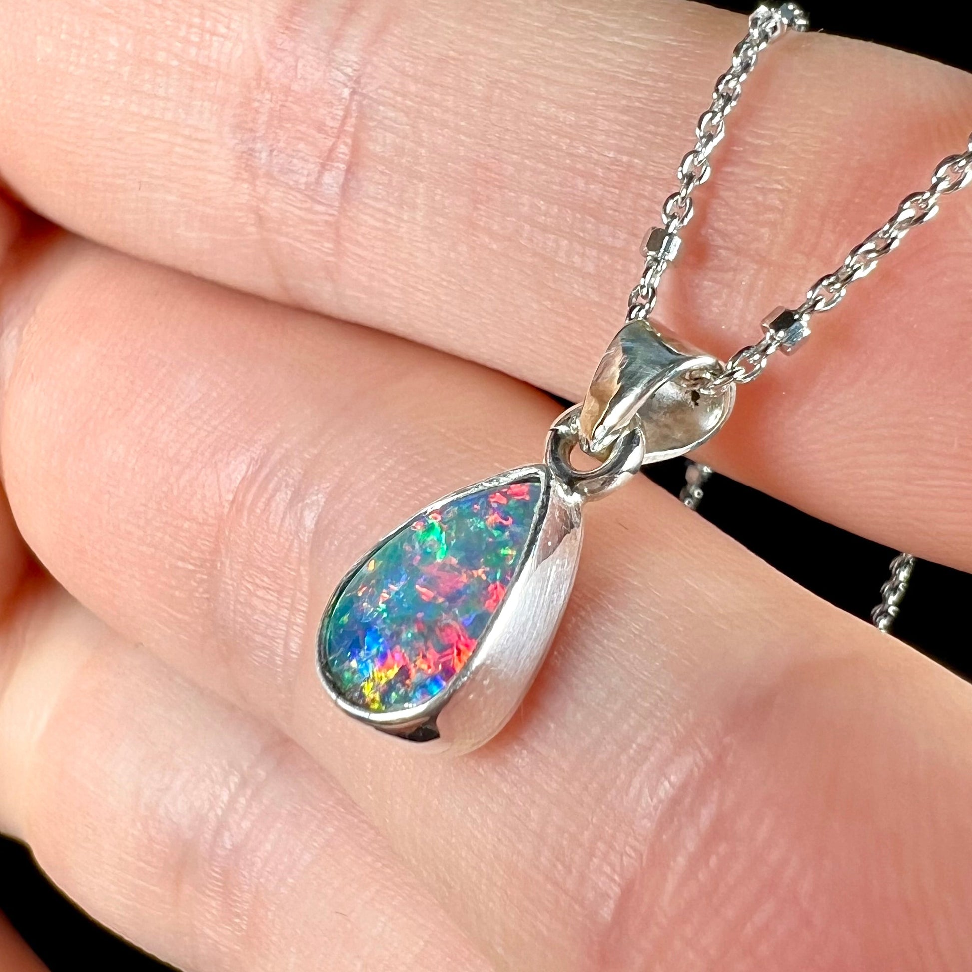 A pear shaped black opal necklace set in sterling silver.  The opal vividly flashes every color of the rainbow.
