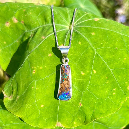 An elongated shaped natural boulder opal necklace in sterling silver.  The opal flashes bright blue and green colors.
