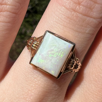 Close-up of women's rectangle cut Australian opal ring in 10k gold, worn on finger under natural sunlight