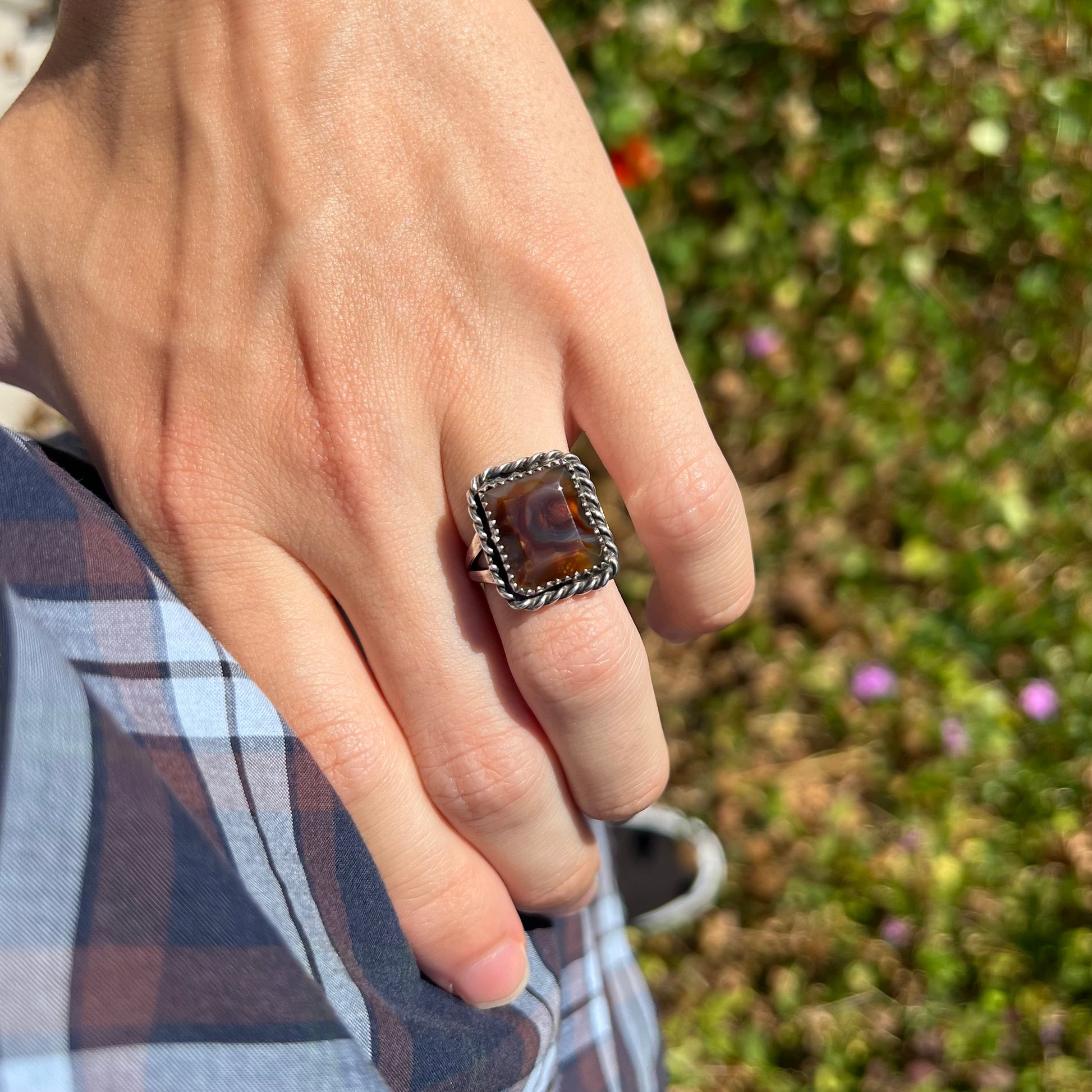 Hand resting on hip while wearing a rectangle shaped silver fire agate ring in natural light.