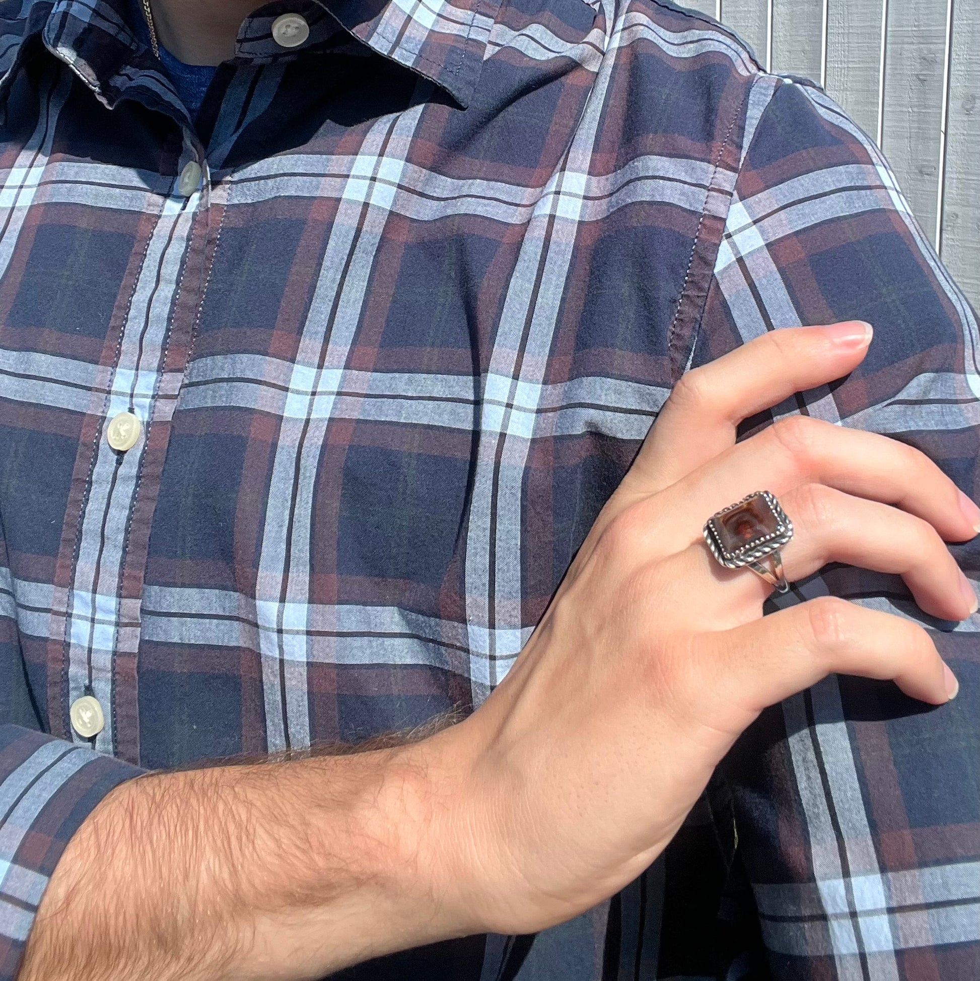 Person's arm crossing body, resting hand on shoulder while wearing a rectangle shaped fire agate ring.