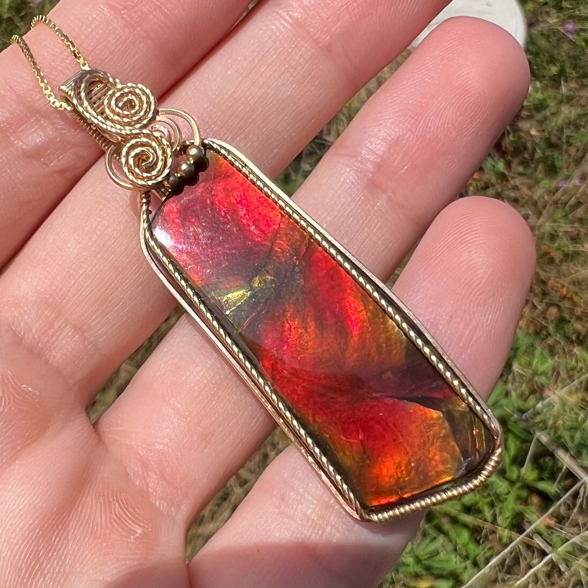 Angled natural light view of a red ammolite necklace held in a hand.
