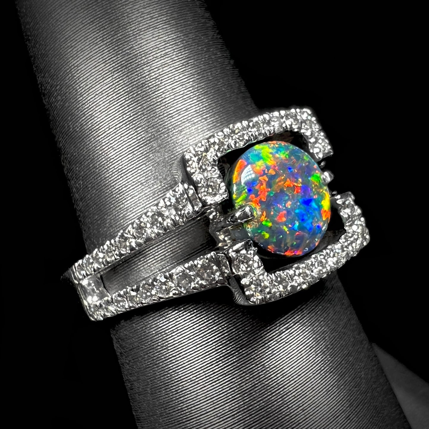 Red flashes play across a round Lightning Ridge black opal engagement ring, set in 14k white gold with diamonds by artist Luciano Bortone.  Angled shot for depth.