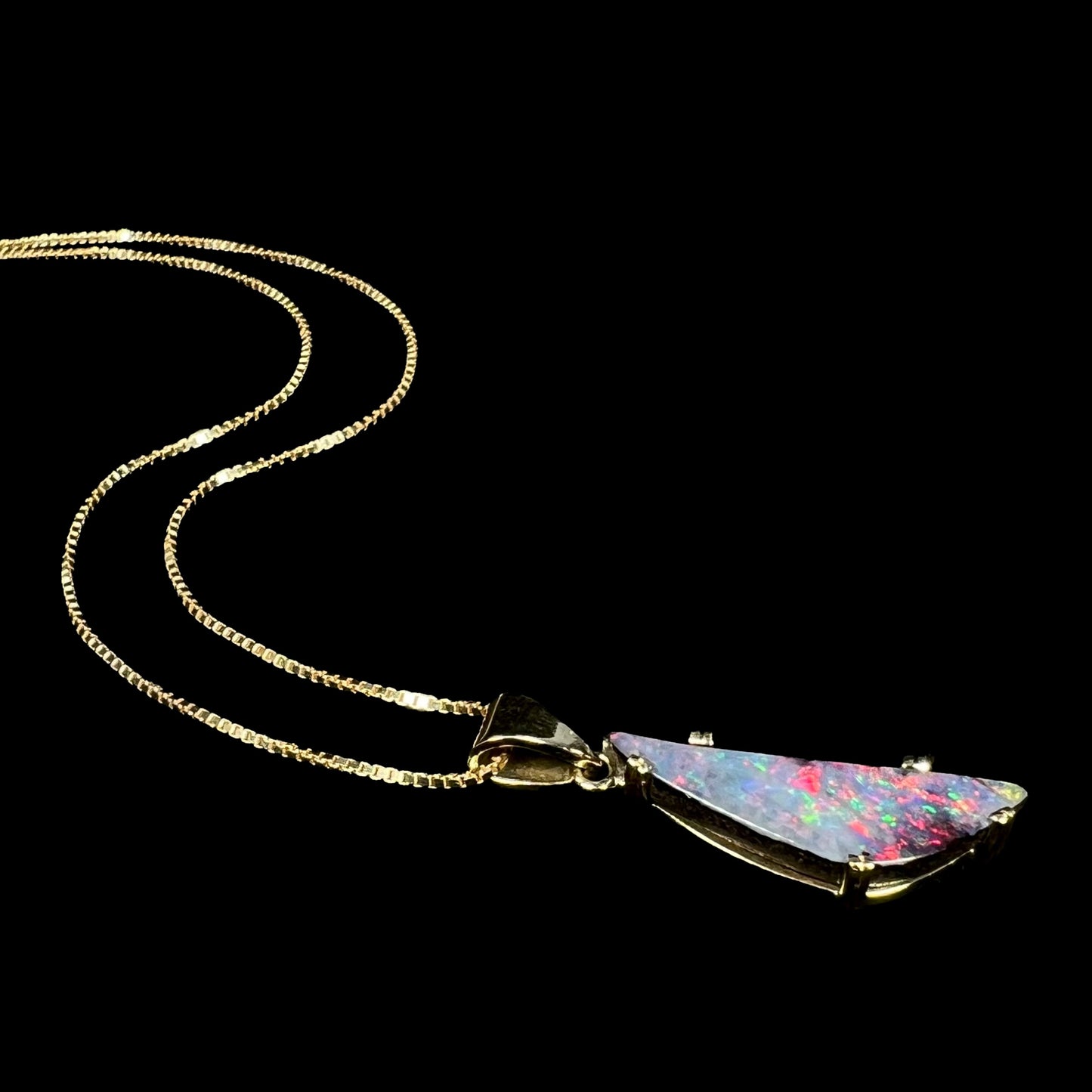 18k gold boulder opal necklace with red flashes of color laying on black background