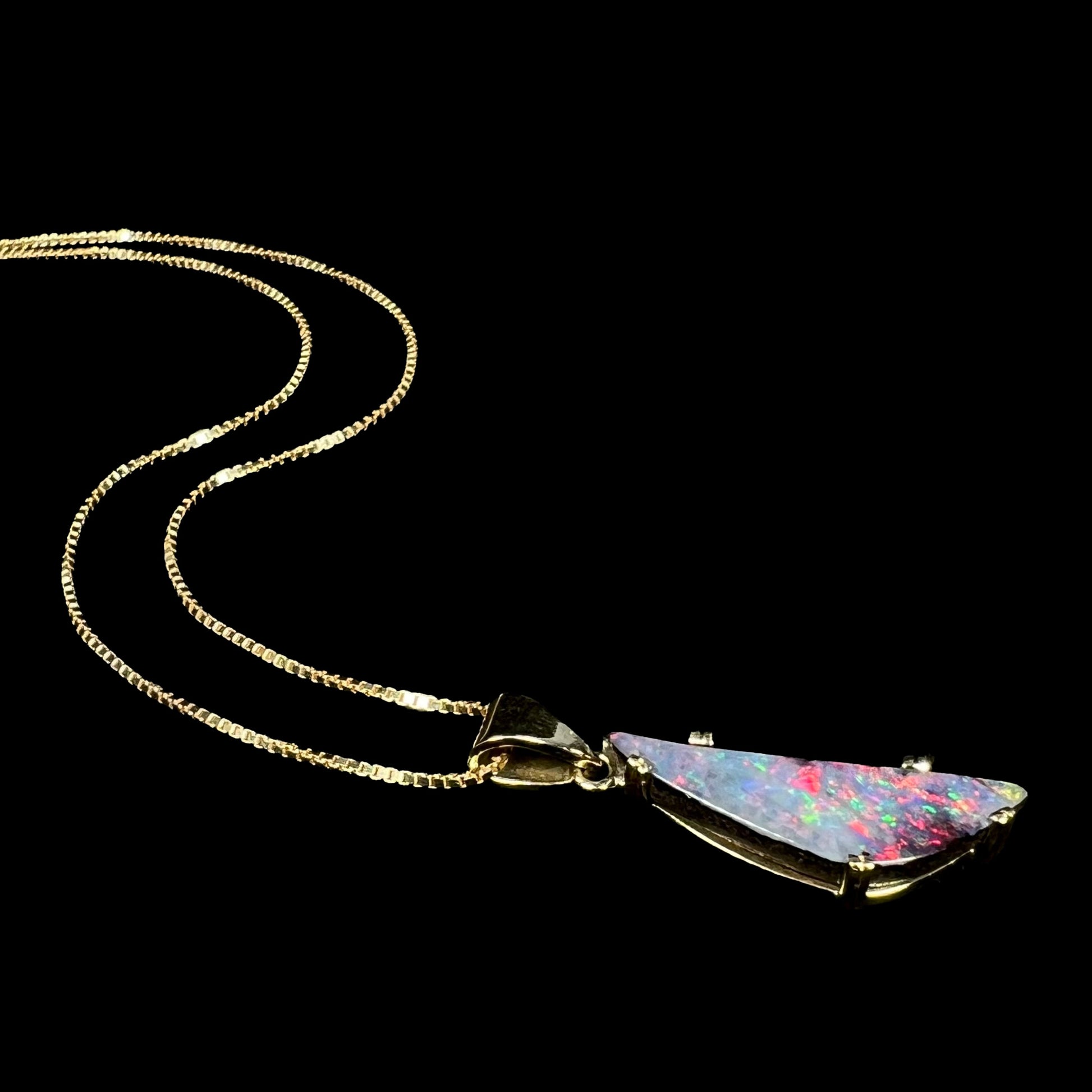 18k gold boulder opal necklace with red flashes of color laying on black background