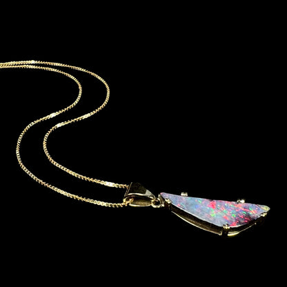18k gold boulder opal necklace with red flashes of color laying on black background