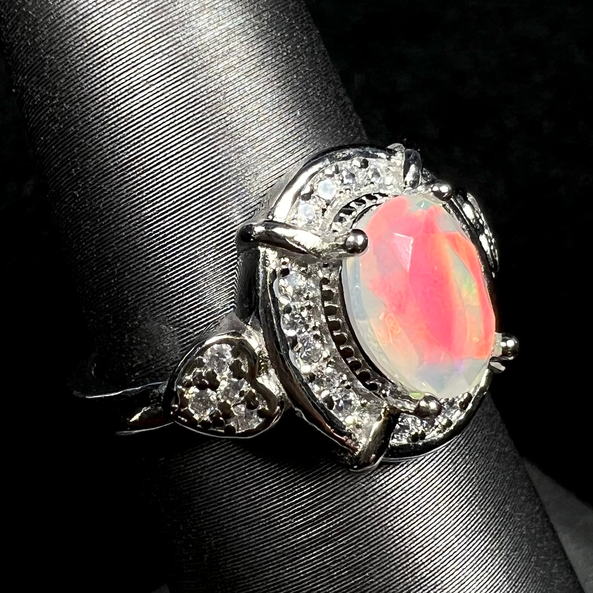 Macro view of silver Ethiopian opal ring with red flash and CZ heart design on display