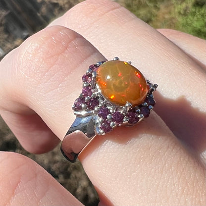 Rolling red colors seen in fire opal mounted in silver garnet-accented ring, worn on finger and viewed close-up in natural light