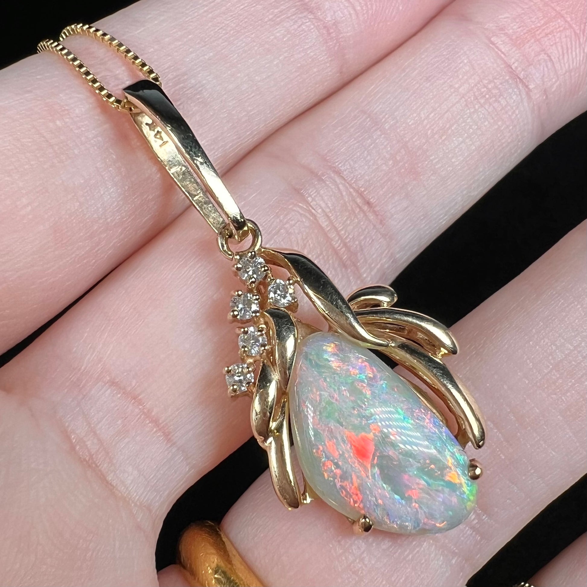 Angled macro view of women's Australian opal and diamond pendant in 14k yellow gold.  The opal shows a large red flash of color.