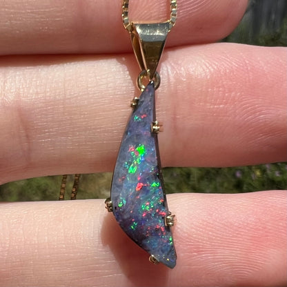 Close-up of Australian boulder opal pendant with red and green flashes in sunlight, resting on fingers
