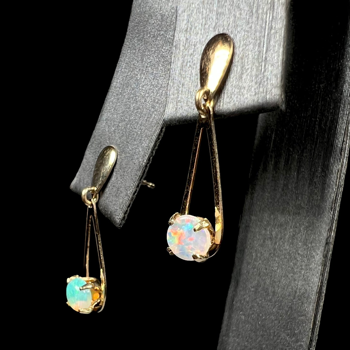 Pair of gold crystal opal dangle earrings shown from angle on earring display.  The opal in focus is red, the opal out of focus is green.