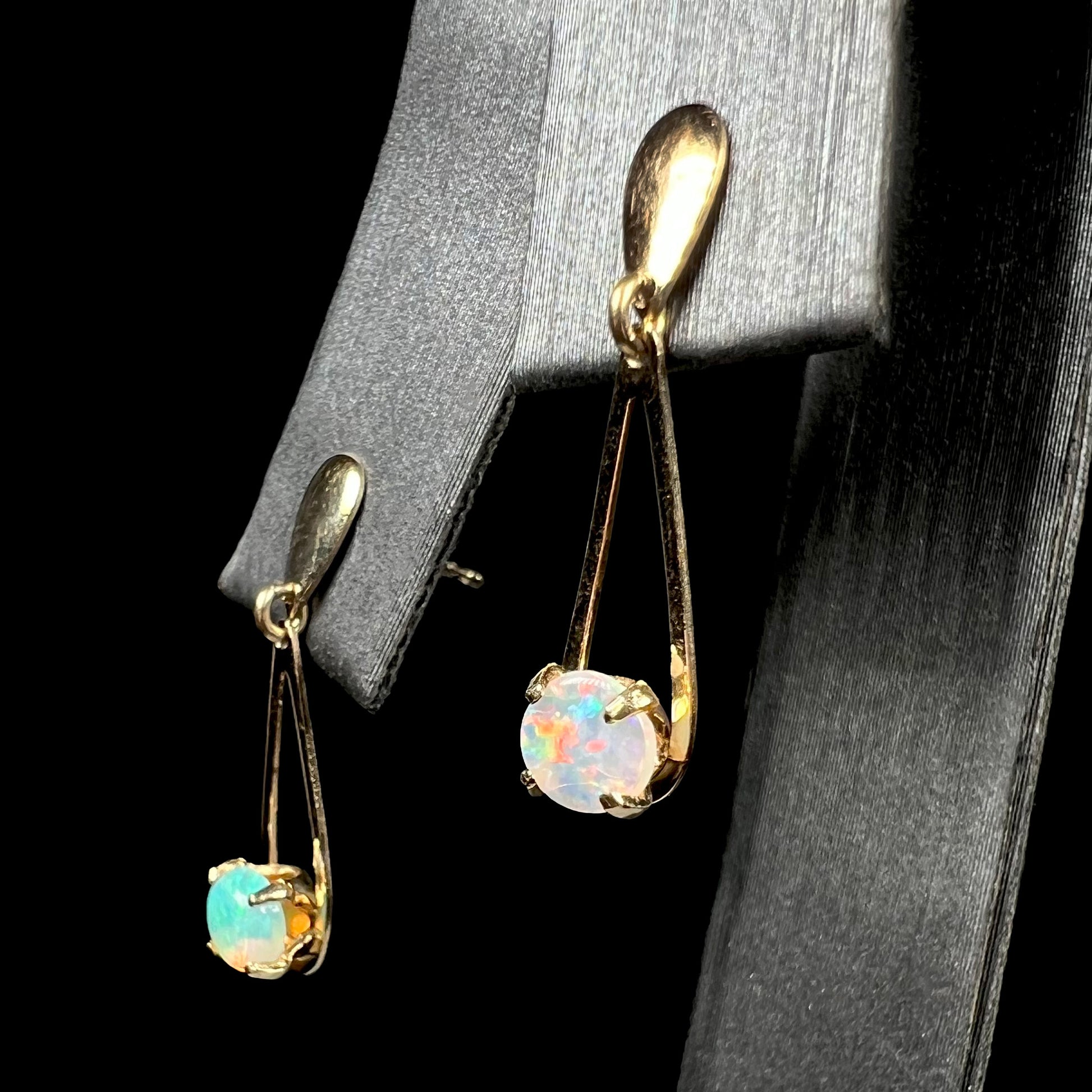 Pair of gold crystal opal dangle earrings shown from angle on earring display.  The opal in focus is red, the opal out of focus is green.