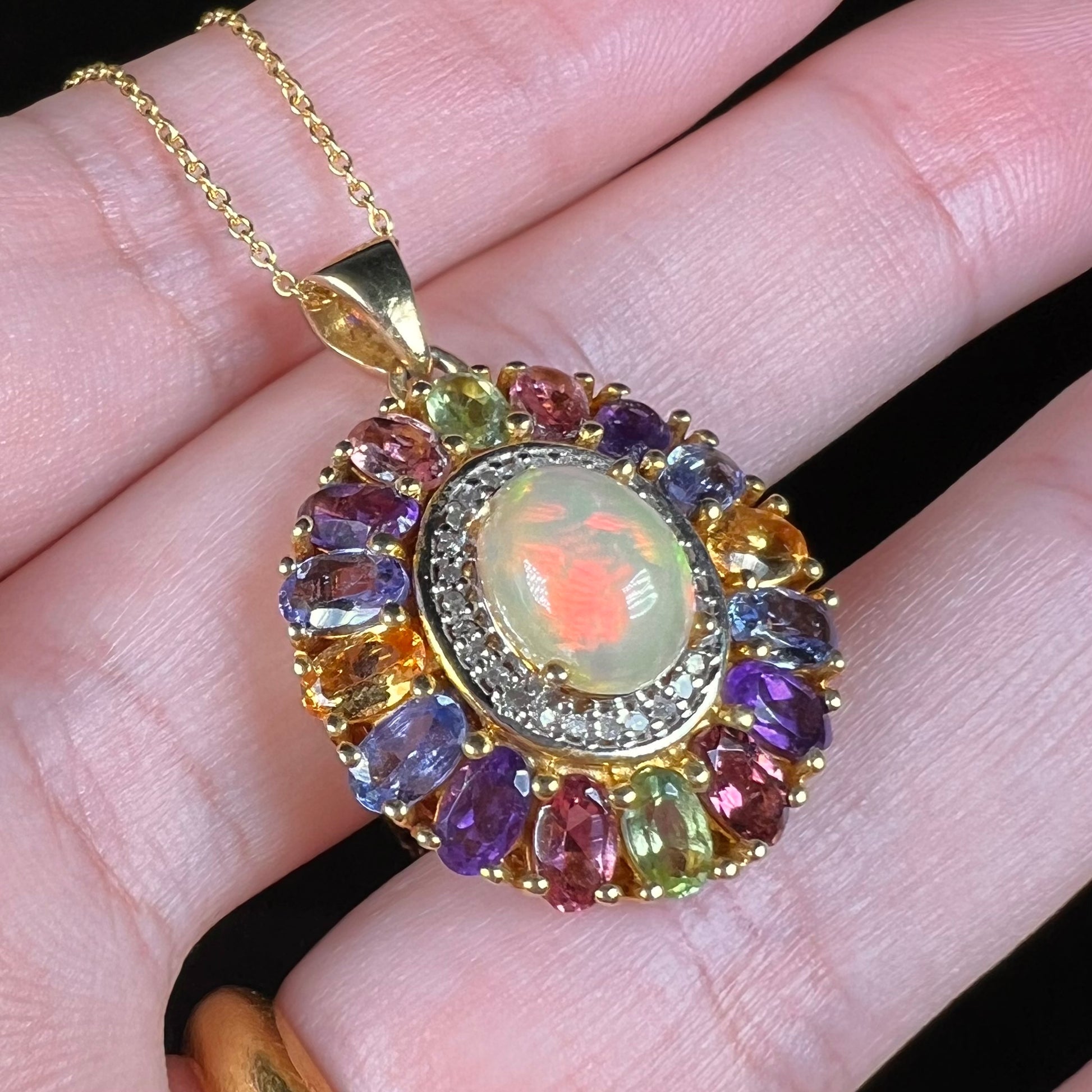 A gold plated sterling silver Ethiopian fire opal and multi-gemstone halo pendant shown close-up from an angle.