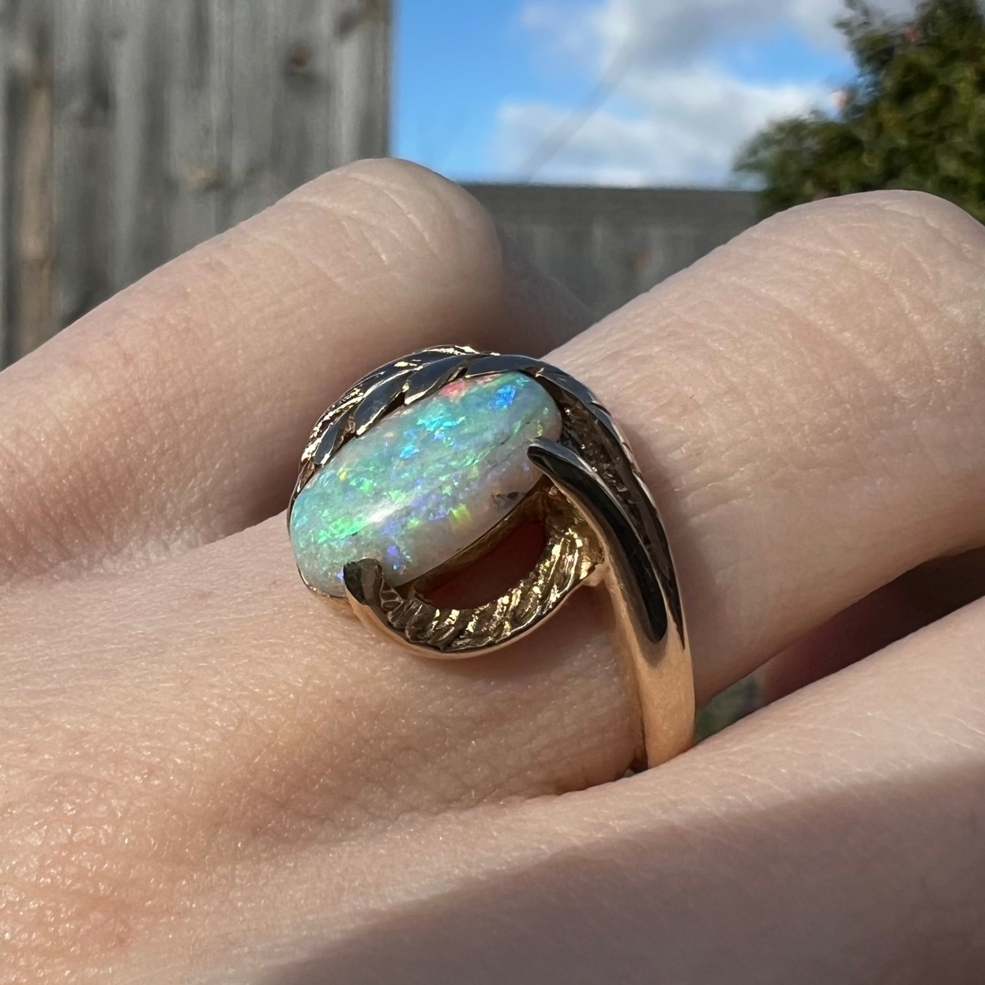 A retro gold opal ring with a leaf and vine design, worn on a finger outside.