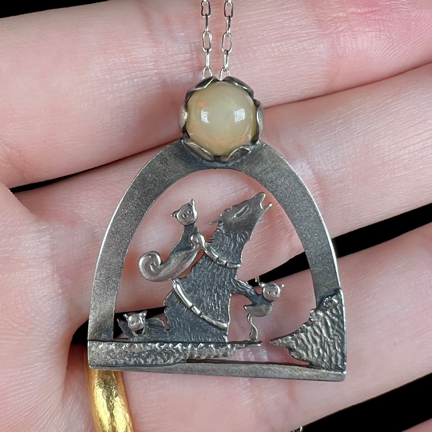Close-up of a sterling silver Ethiopian opal wolf and cat design necklace, held in a hand.