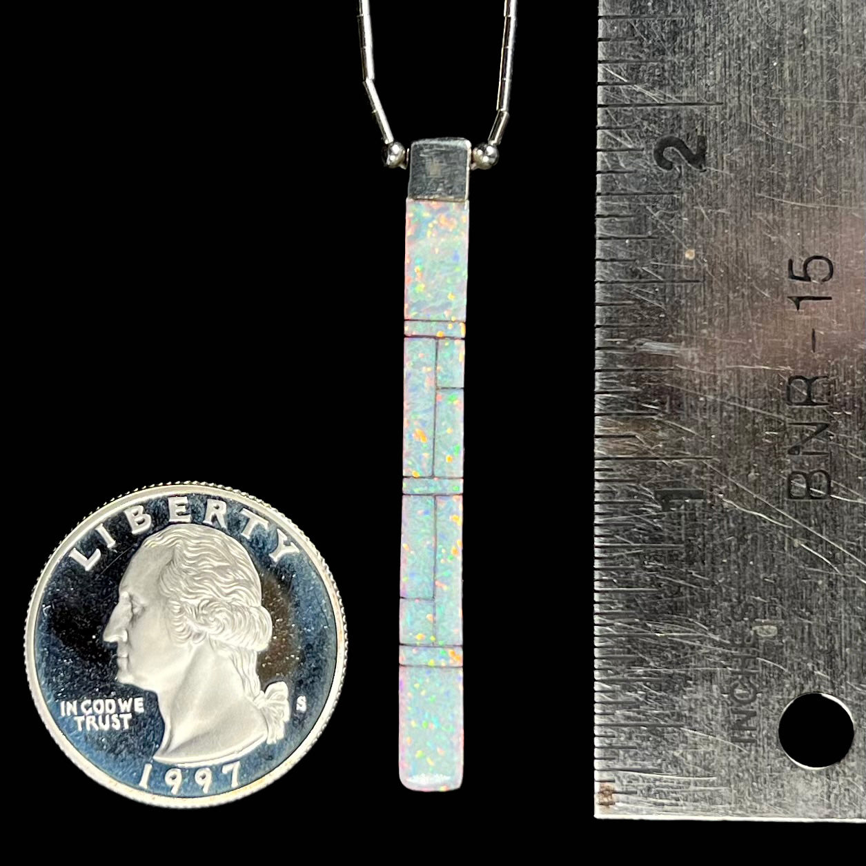 A reversible Navajo inlay pendant next to a quarter and ruler for size comparison, measuring approximately 2 inches with the bail.