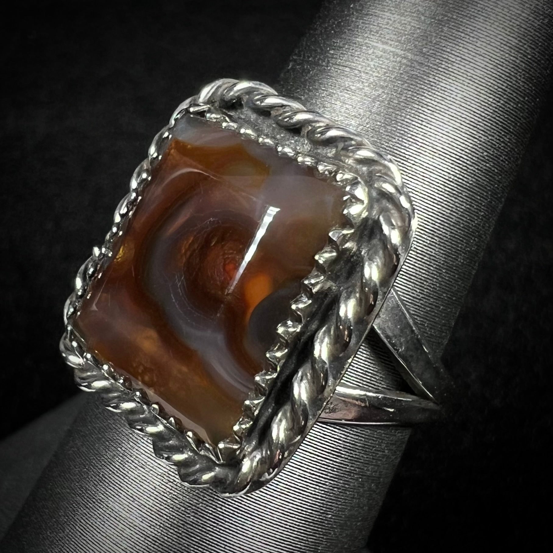A silver rope design fire agate ring with a split shank shown from an angle.