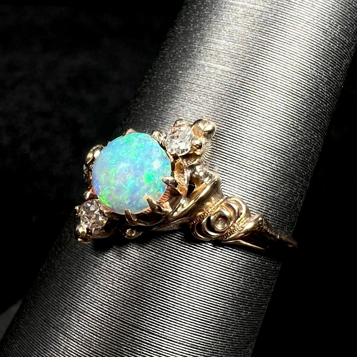 Angled close-up of rose design on shoulder of Art Nouveau 10k gold opal and Old European Cut diamond ring, shown on ring display