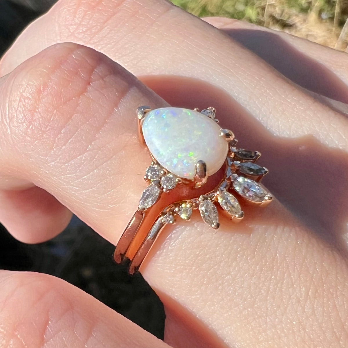 Women's 14k rose gold Australian opal and moissanite-accented wedding ring set worn on hand in natural light