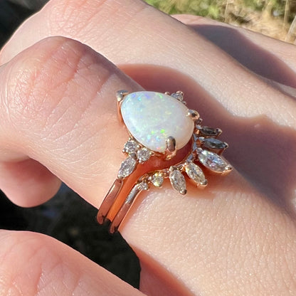 Women's 14k rose gold Australian opal and moissanite-accented wedding ring set worn on hand in natural light