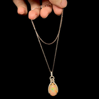 Hand dangling a rose gold pear shaped Ethiopian opal and diamond necklace by Le Vian from its cable-style chain against a black background.