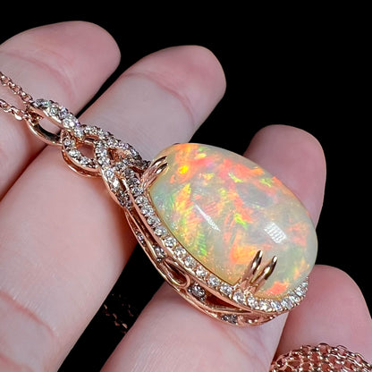 Rose gold Ethiopian opal and diamond pendant shown resting on fingers from an angle against a black background.