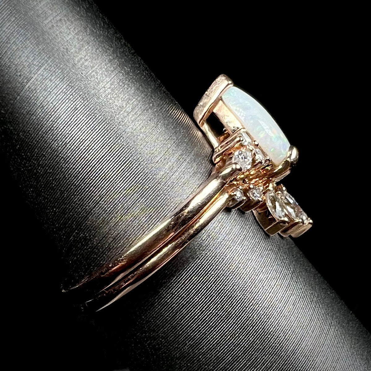 Side view of rose gold opal and moissanite engagement ring set on display, focused on rings' shanks