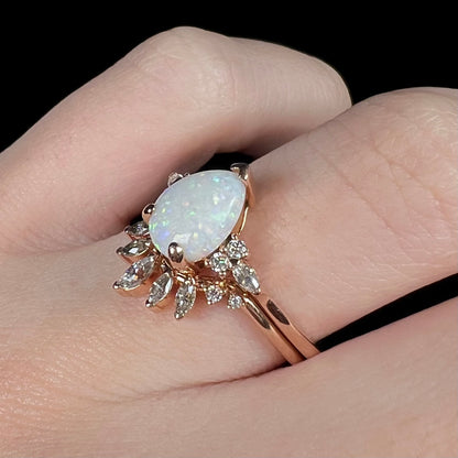 A rose gold wedding ring set with a large white opal and small moissanites, shown worn on a hand against a black background.