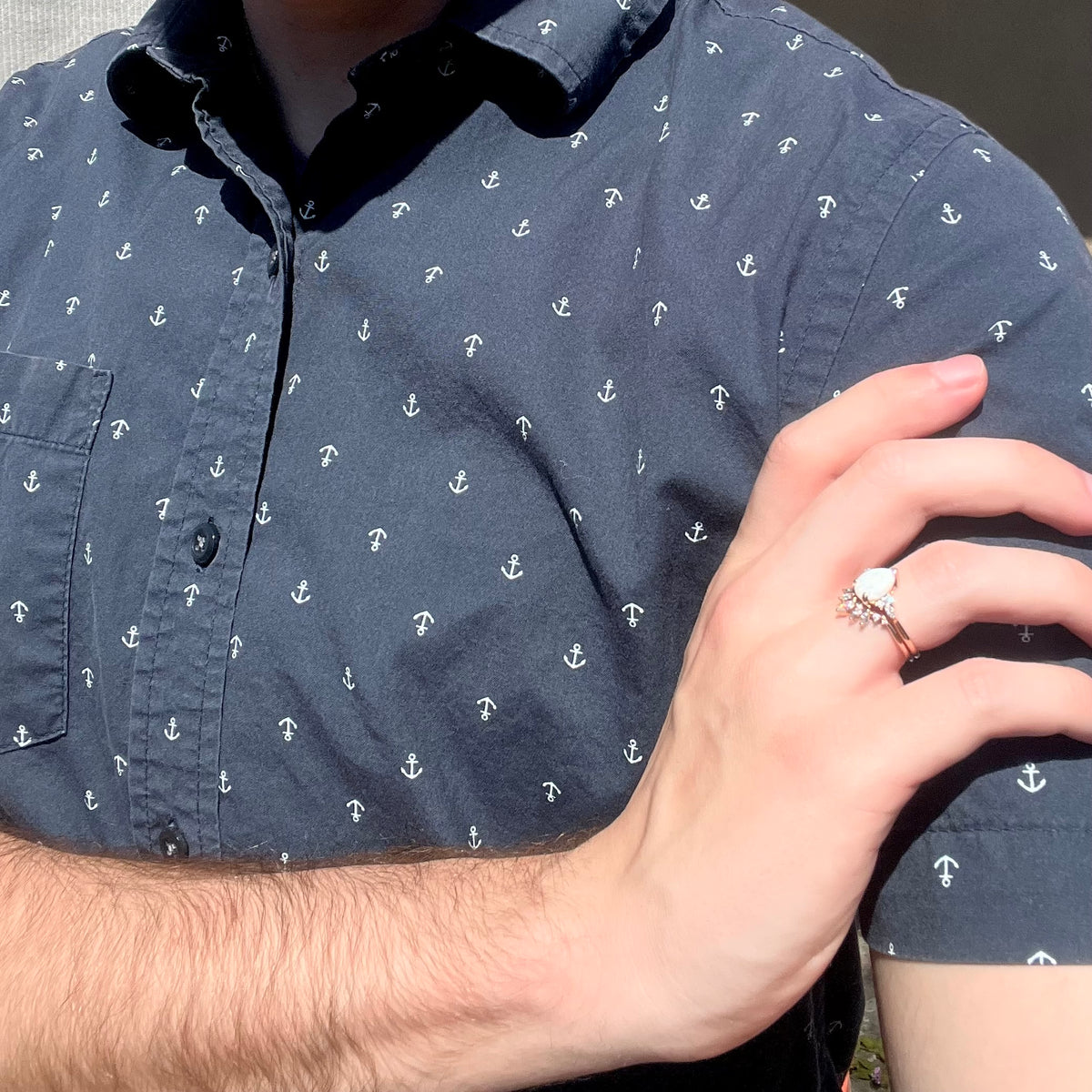 Close-up of person resting hand on shoulder in sunlight while wearing a rose gold opal and moissanite wedding ring set
