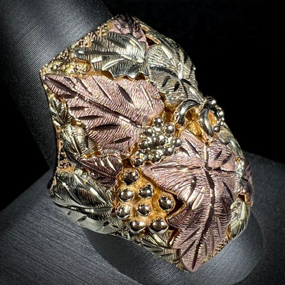 A men's solid gold ring.  The ring is Black Hills gold featuring a grapevine and leaf motif with rose and green gold designs.