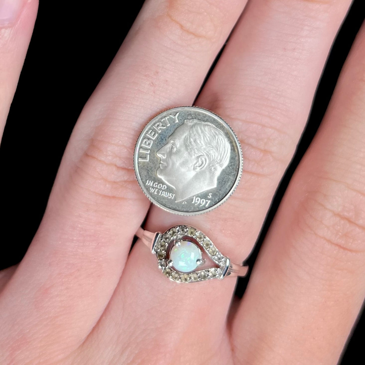 Close-up of round Australian white opal and smoky quartz ring in sterling silver, worn on hand next to US dime coin