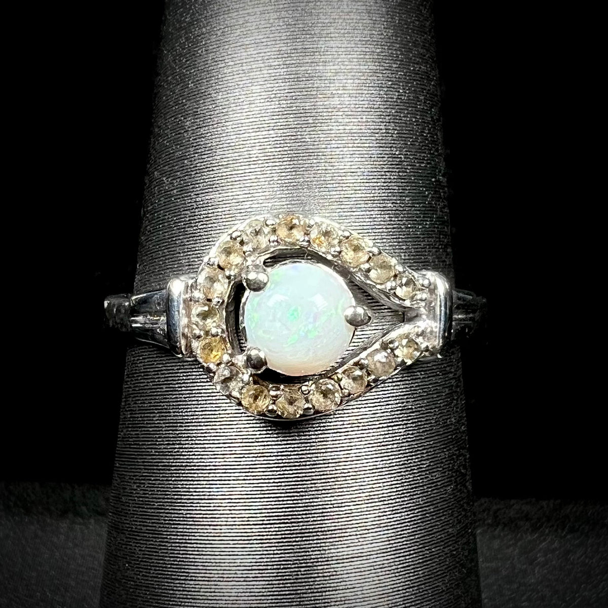 Close-up front view of round Australian white opal women's ring with smoky quartz halo design in sterling silver, shown on ring display
