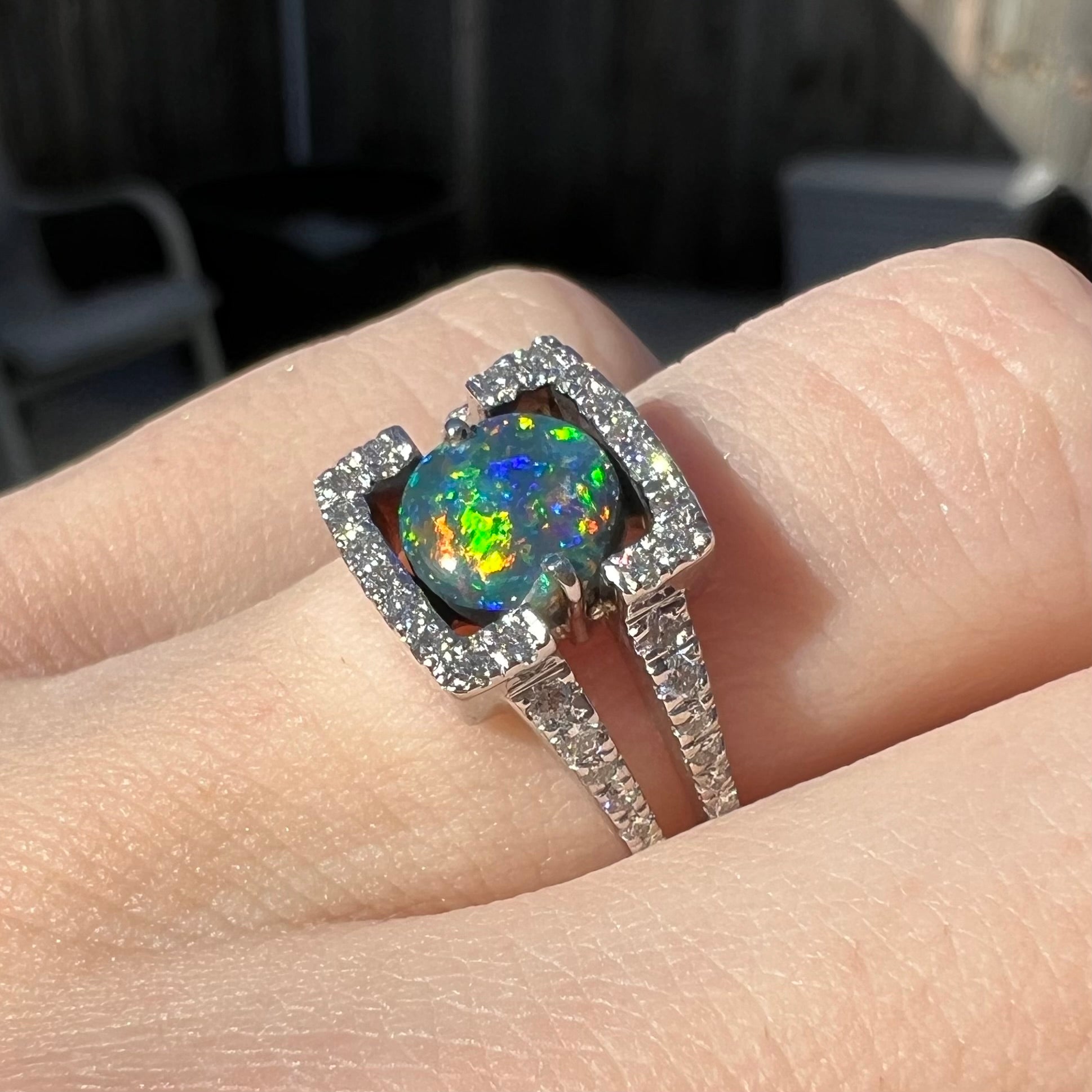 A round black opal and diamond-accented ring by designer Luciano Bortone, worn on a hand.