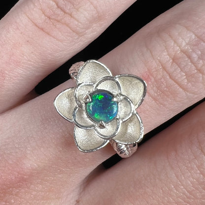 Close-up of silver flower ring set with round Australian black opal, worn on finger