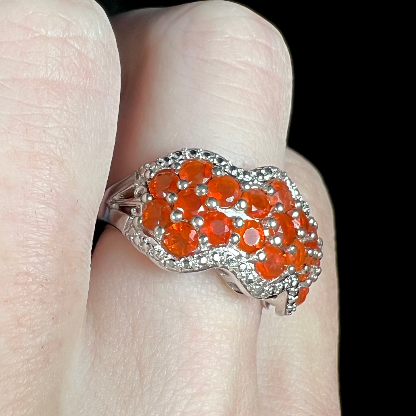 Close-up angled view of a women's faceted round cut Mexican fire opal cluster ring in sterling silver, worn on a finger under LED light.