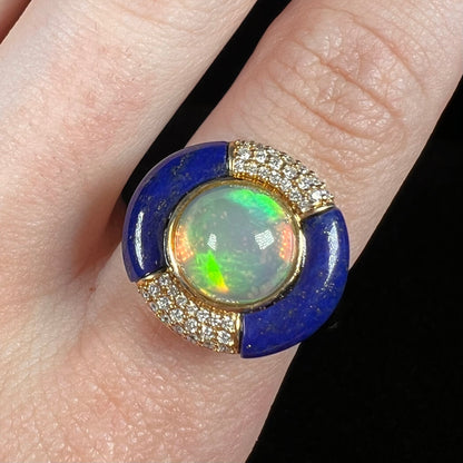 Close-up of a round Ethiopian fire opal women's ring by Cirari, worn on a finger under cool LED light.  The opal has green flashes of color.