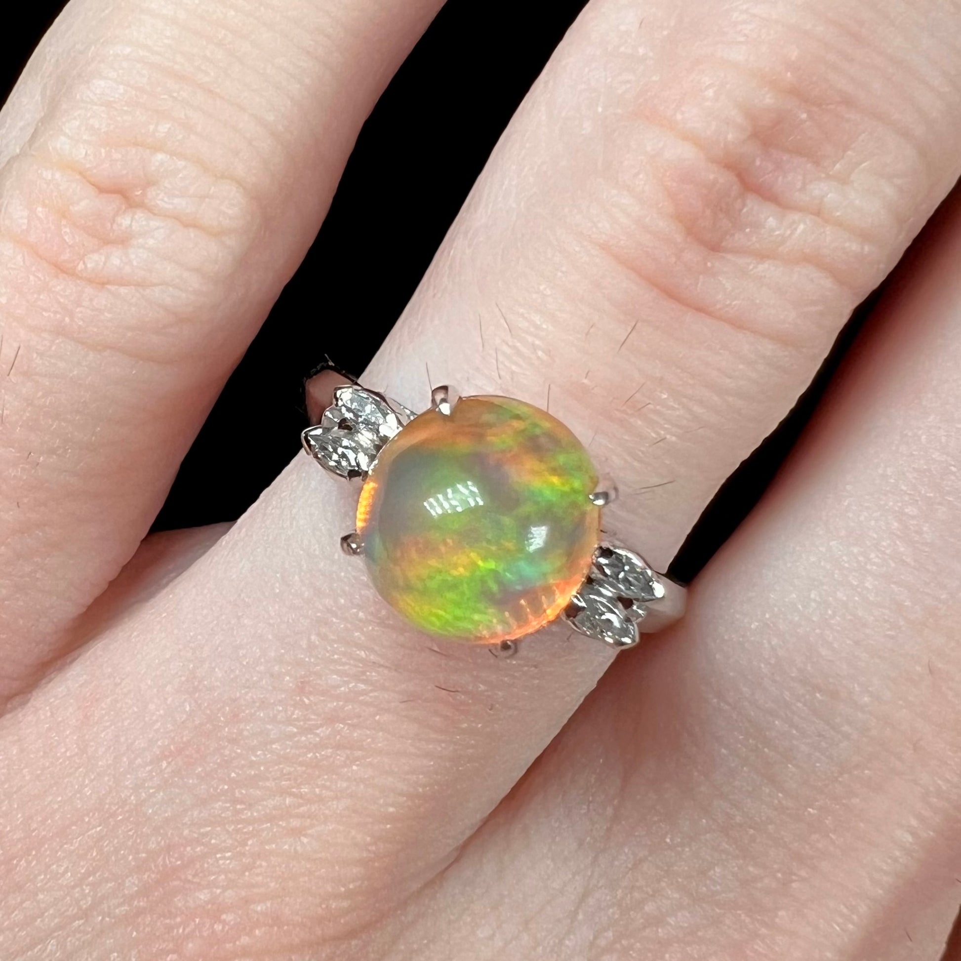 Close-up of a round engagement ring worn on a finger, featuring a 2.28ct Mexican fire opal with green fire in platinum.