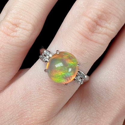 Close-up of a round engagement ring worn on a finger, featuring a 2.28ct Mexican fire opal with green fire in platinum.