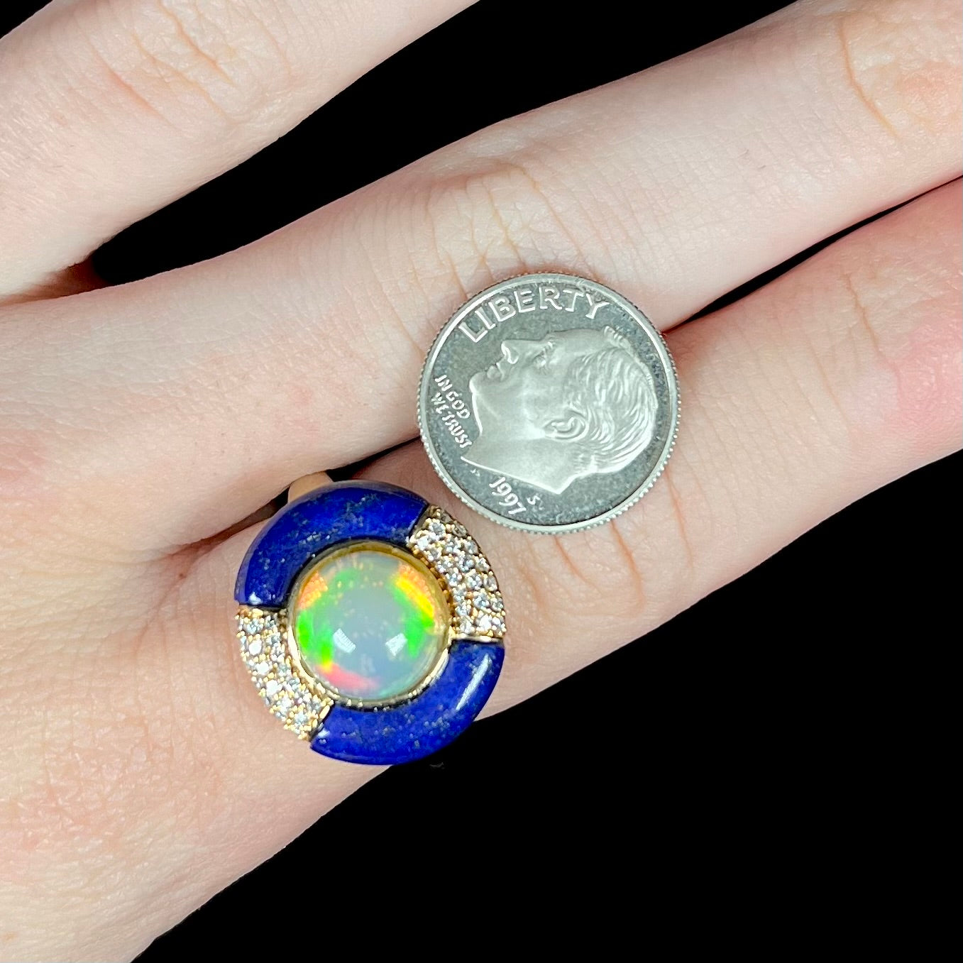 A dime-sized round fire opal, lapis lazuli, and diamond women's ring in 14k gold, worn on a finger next to a US dime coin for scale.
