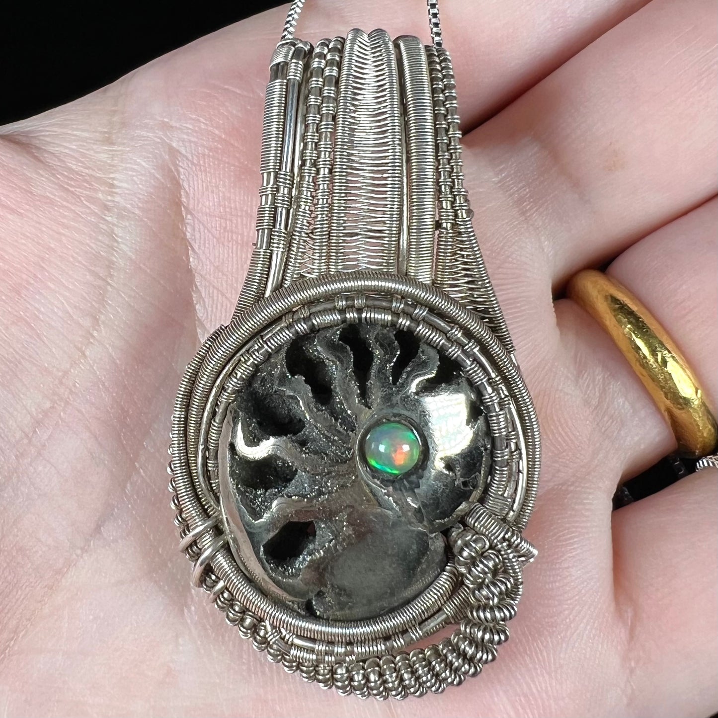 Close-up macro view of a man's ammonite wire wrap pendant accented by a round Ethiopian opal, held in a hand.