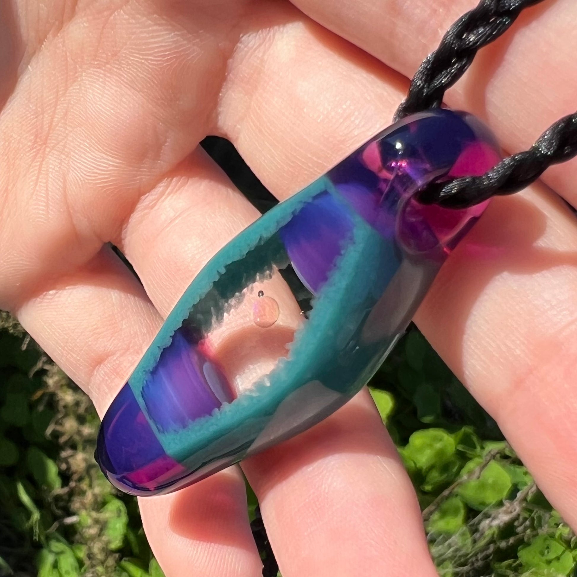 Angled view of a clear, round opal disk in a glass pendant, shown close-up from an angle in a hand under natural sunlight.
