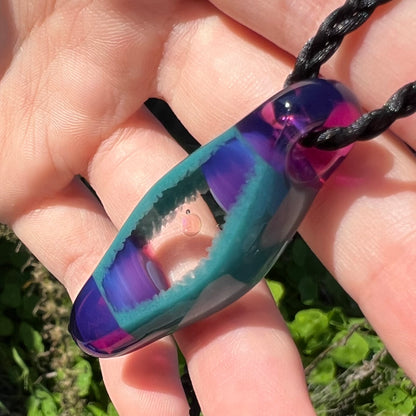 Angled view of a clear, round opal disk in a glass pendant, shown close-up from an angle in a hand under natural sunlight.