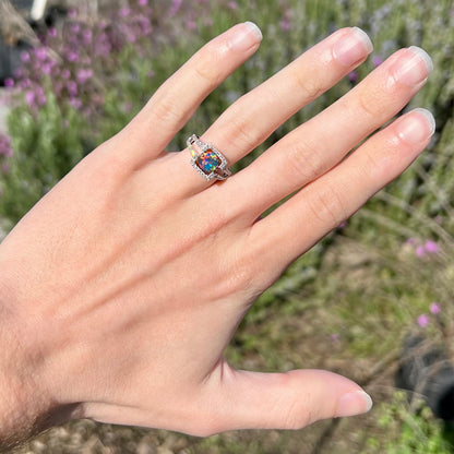 A round black opal engagement ring with red fire worn on a hand in the sunlight.