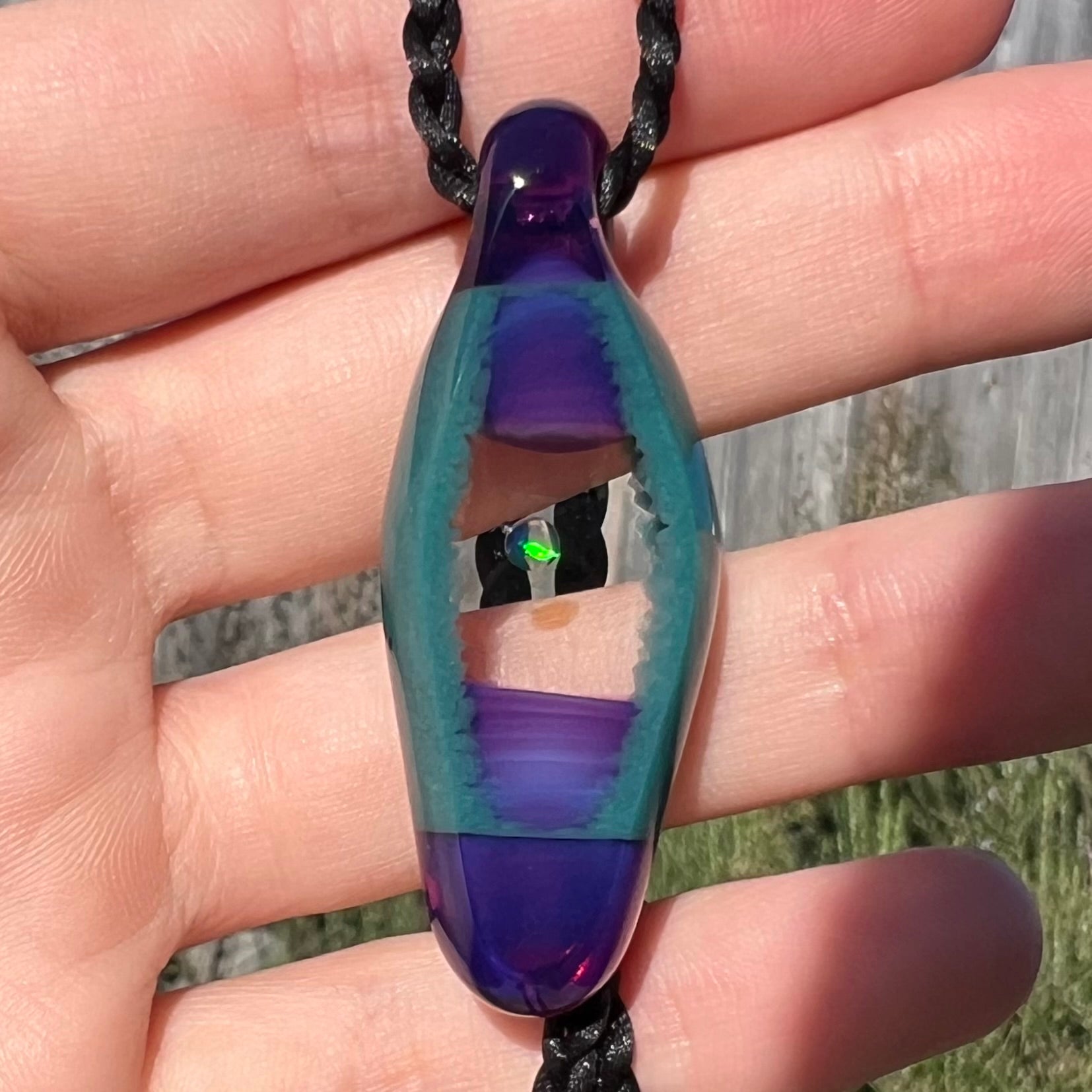 Close-up of a round lab-created opal in boro glass pendant by Nathan Snyder, shown in a hand and held in the sunlight.