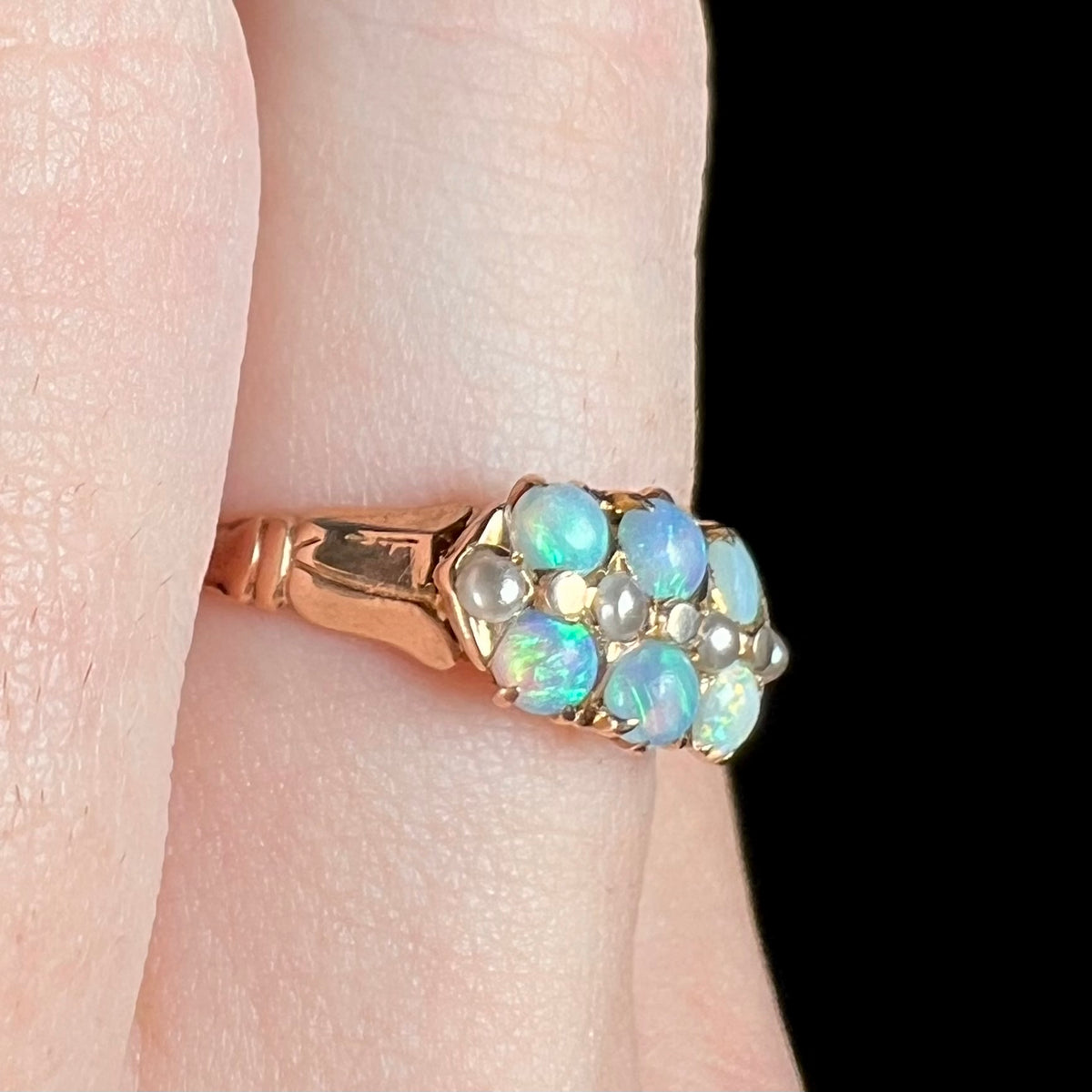 Women's gold Victorian ring set with six round opals and four pearl accents, worn on finger and shown close-up from angled view