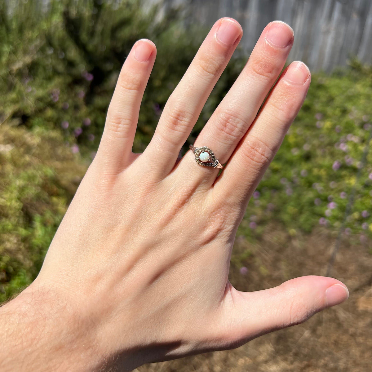 Round Australian opal and smoky-quartz halo design ring worn on hand under natural sunlight