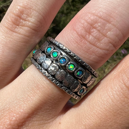 Close-up front view of an opal spinner ring set with round opals, worn on a finger in the sunlight.