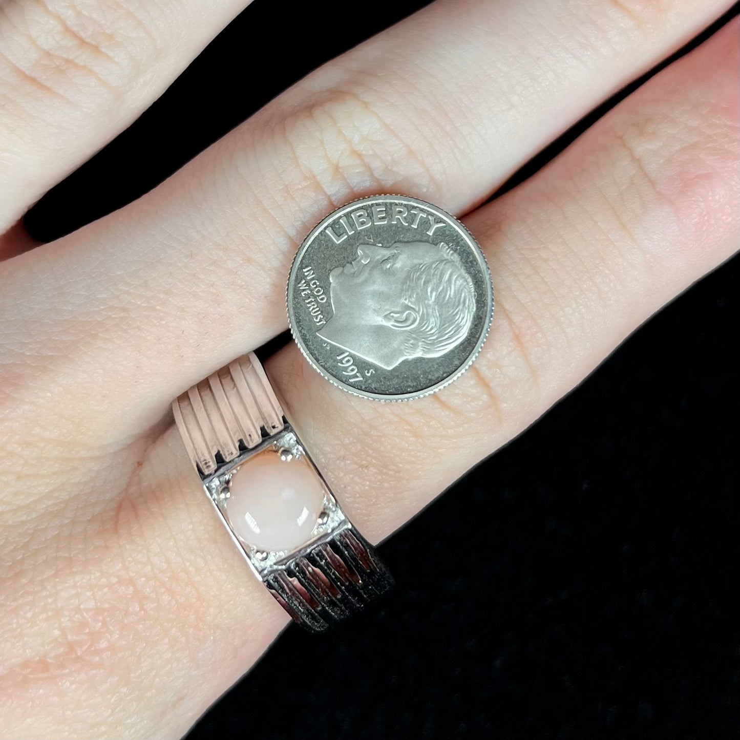 Round pink opal ring in silver on finger next to US dime coin for scale