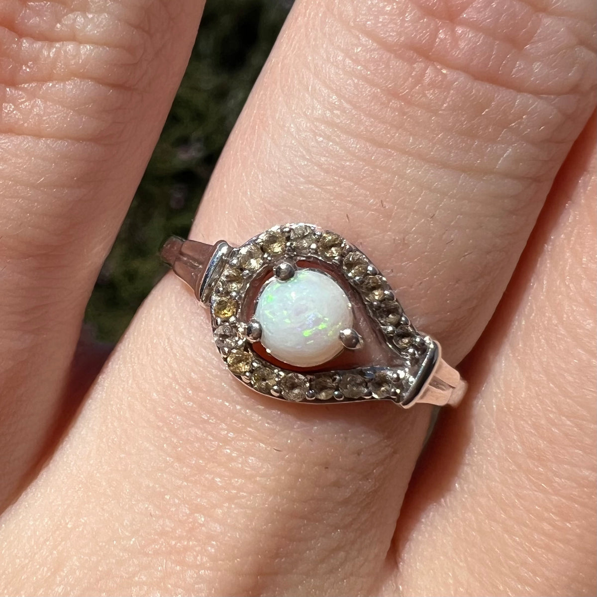 Close-up of a round white Australian opal ring with smoky quartz accents in sterling silver, worn on finger in sunlight; the opal has green colors